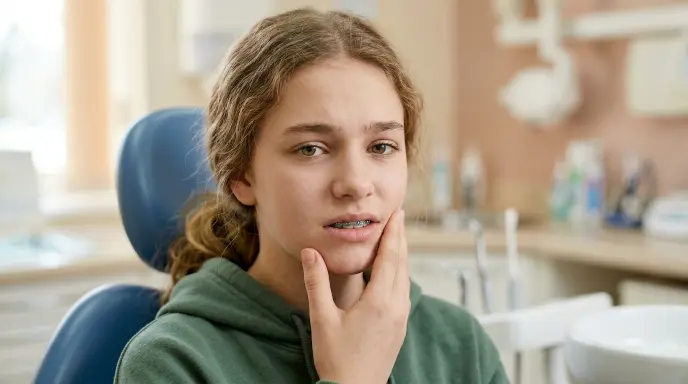 Teenager wearing braces holding jaw with mild discomfort, showing typical soreness after orthodontic treatment
